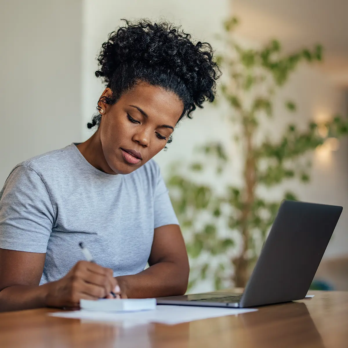 Young woman writing on paper next to her laptop computer